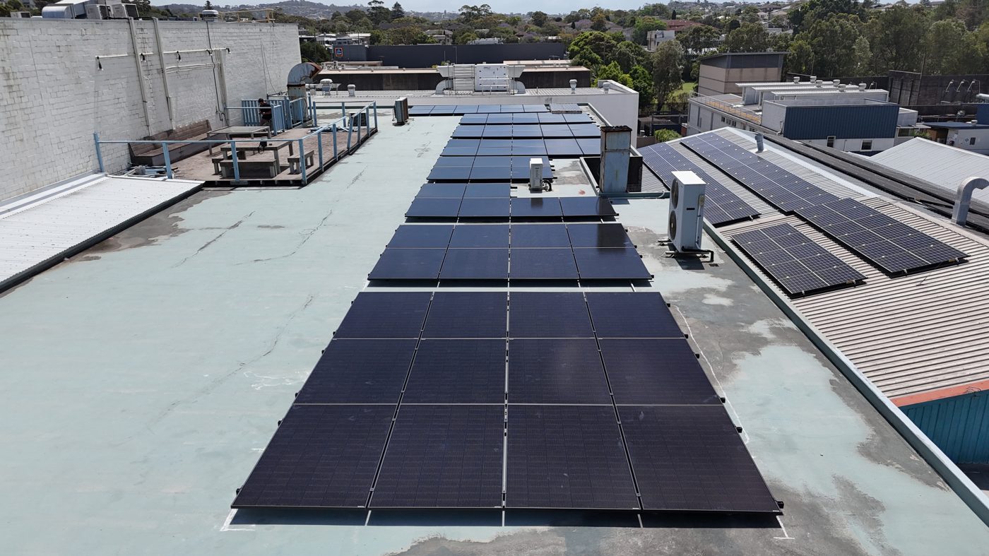 Aerial view of a dense commercial rooftop solar array on a coastal Sydney business