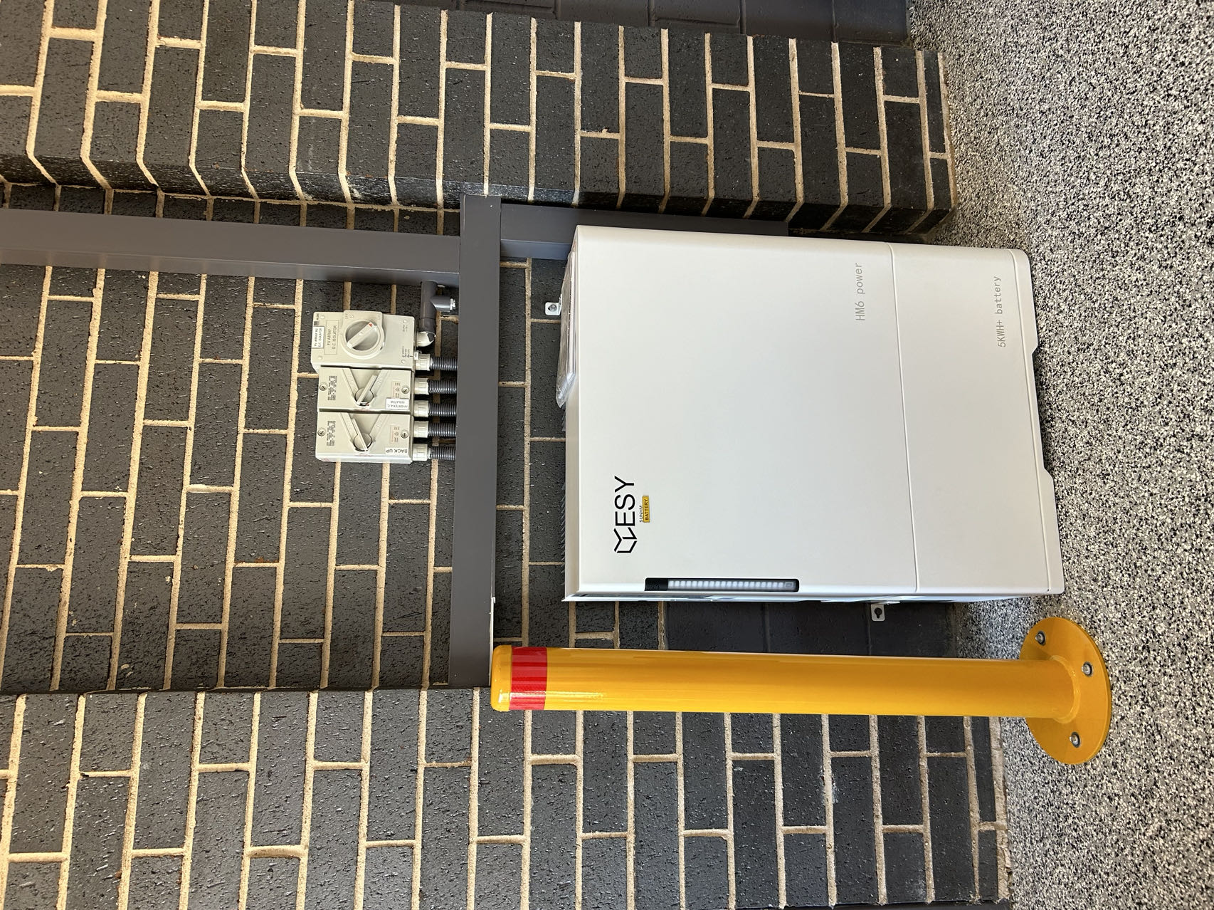 Installed ESY Sunhome battery unit with hybrid inverter mounted on an exterior brick wall