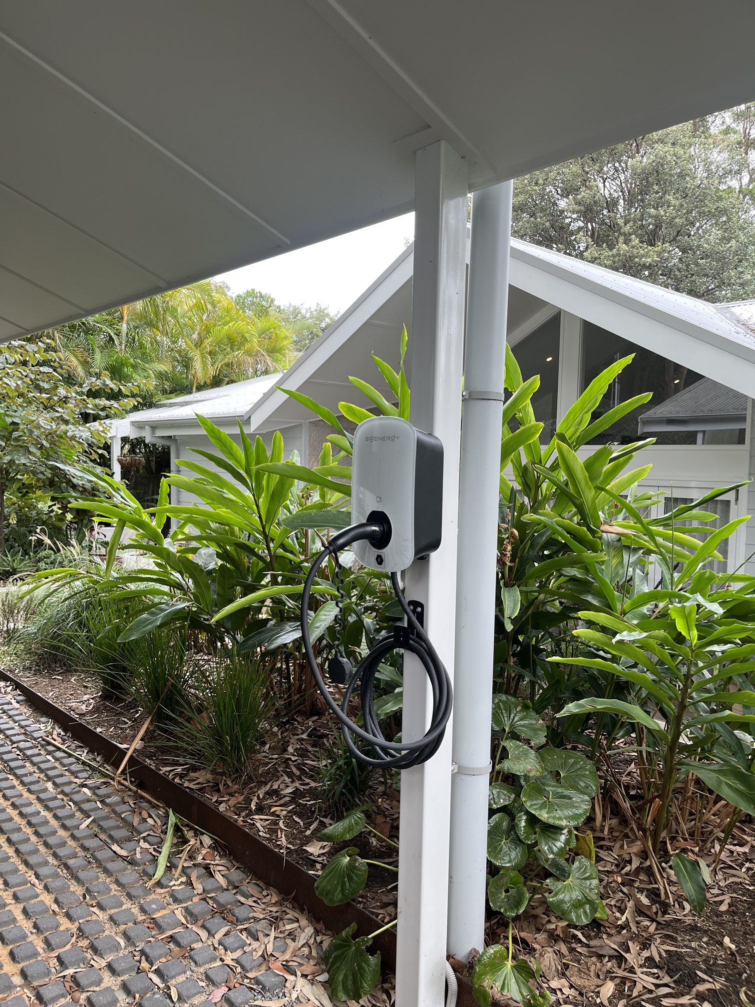 EV charger installed on a carport post surrounded by garden greenery