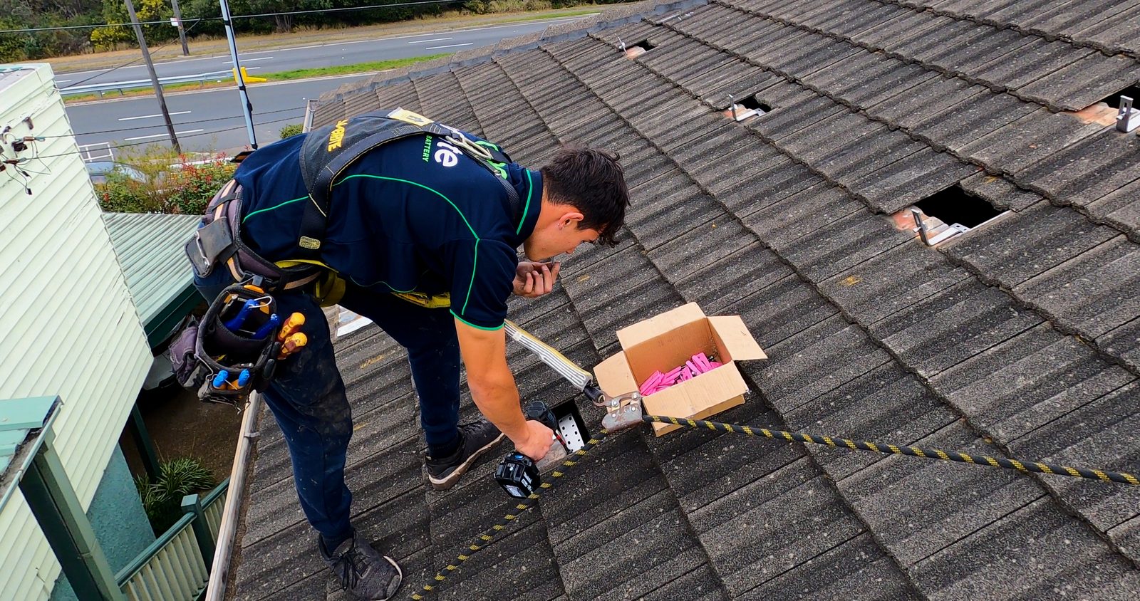 A harnessed installer fitting a roof mounting bracket on a tiled residential roof